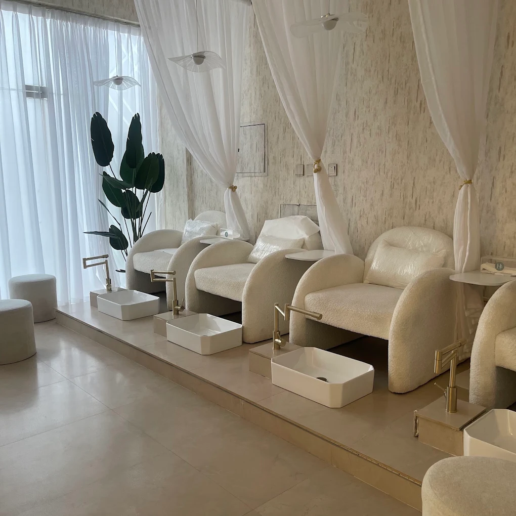 H Beauty pedicure lounge with cream chairs, sheer curtains and gold fixtures